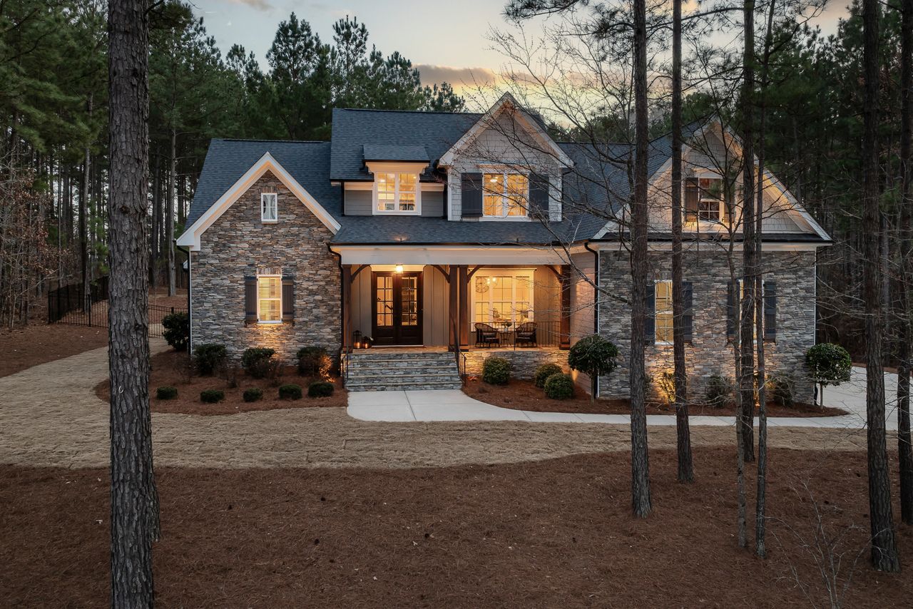 The Art of Drawing Readers In: Your attractive post title goes here Charming modern stone house nestled among tall pine trees at dusk, emitting a warm glow.